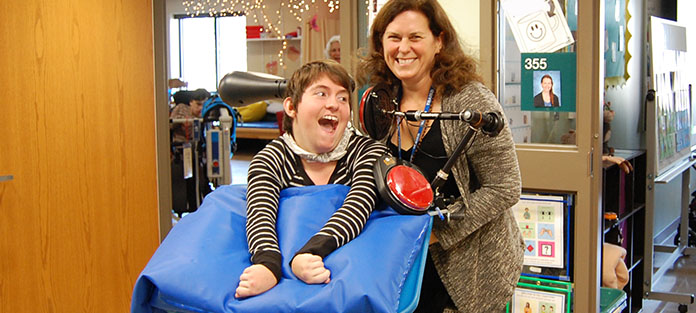 Smiling student with Physical Therapist with an assistive technology device for speaking