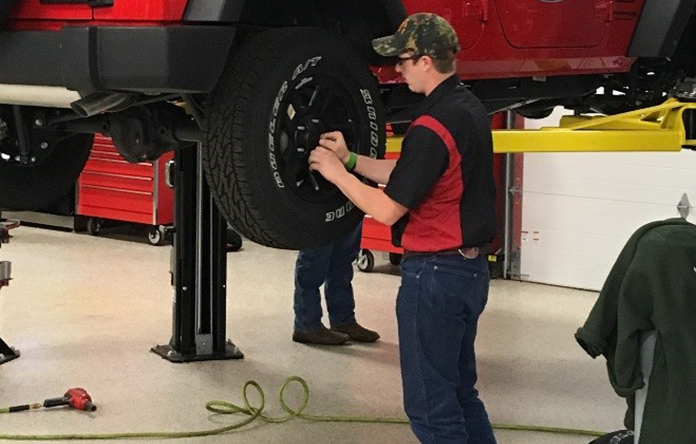 Male student auto technician securing a wheel on a vehicle.